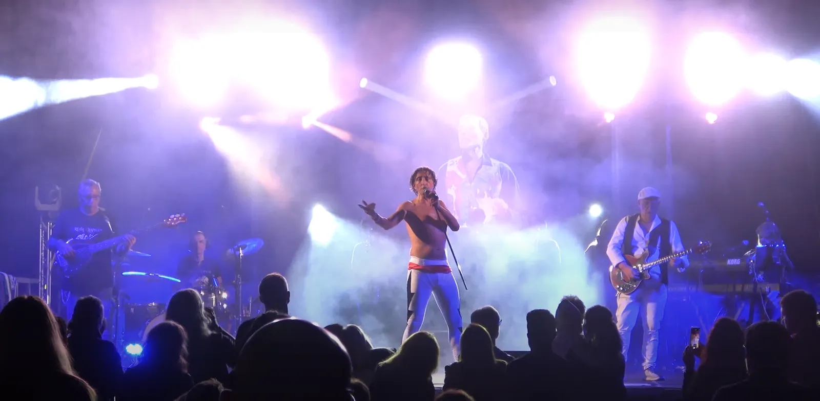 Il cantante in mezzo alla band, sotto luci blu